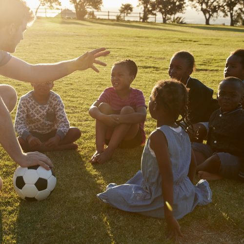 Elementary school kids and teacher sitting with ball in field