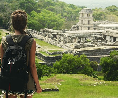 Woman with backpack beside ancient Mayan ruins